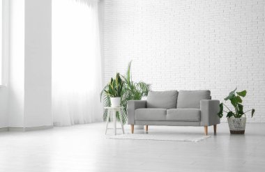 Oturma odasındaki beyaz tuğla duvarın yanındaki kanepe ve bitkiler.