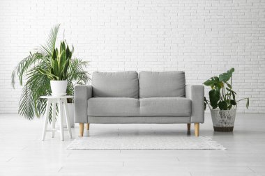 Oturma odasındaki beyaz tuğla duvarın yanındaki kanepe ve bitkiler.