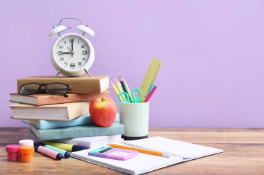 Renk duvarına karşı ahşap masa üzerinde gözlüklü ve alarmlı farklı kırtasiye malzemeleri.