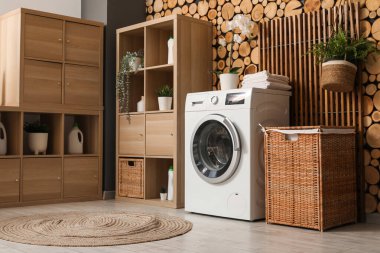 Çamaşır makinesi, raf ünitesi ve odasındaki ahşap duvarın yanındaki çamaşır sepeti.