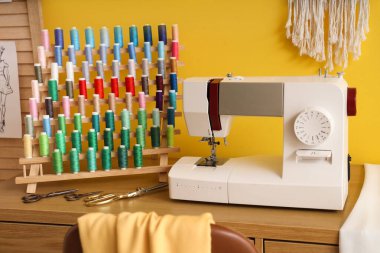 Atölyedeki terzi masasında iplik makaralı dikiş makinesi.