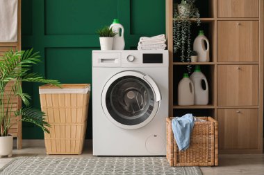 Çamaşır makinesi, raf ünitesi ve yeşil duvarın yanındaki çamaşır sepeti.