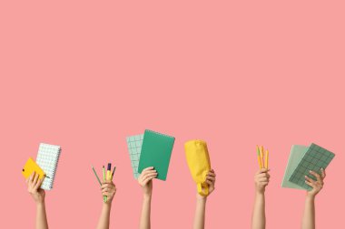 Pembe arka planda farklı kırtasiye malzemesi olan kadın elleri