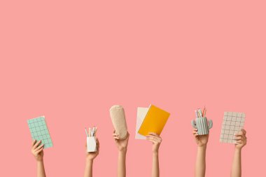 Pembe arka planda farklı okul malzemelerine sahip kadın eller.