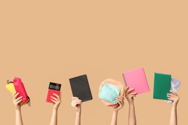 Bej arka planda farklı okul malzemelerine sahip kadın eller.