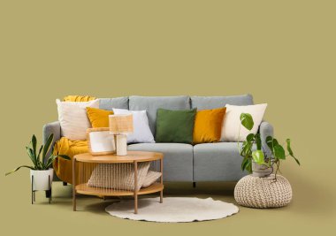 Pouf, masa ve yeşil arka planda bitkiler olan gri kanepe.