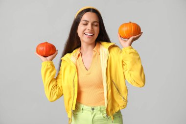 Gri arka planda taze balkabakları olan güzel genç bir kadın.