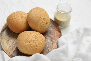 Tahta bir tabak taze çörek ve beyaz arka planda susam tohumları.