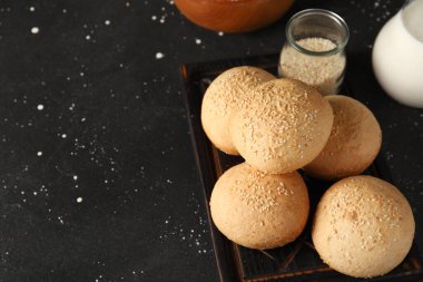 Tahta tahtada siyah zemin üzerinde susam tohumları olan taze çörekler.