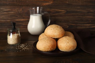 Susam tohumlu taze çörekler ve tahta arka planda bir sürahi süt.