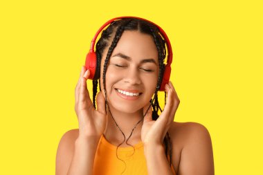 Genç Afro-Amerikalı kadın sarı arka planda müzik dinliyor.
