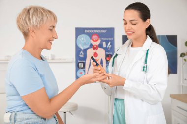 Kadın endokrinolog klinikte olgun bir kadının kan şekerini ölçüyor.