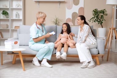 Evde küçük bir kız ve annenin sıcaklığını ölçen kadın bir çocuk doktoru.