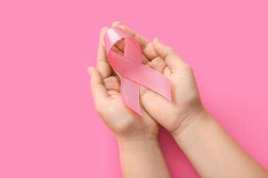 Renkli arka planda pembe farkındalık kurdelesi olan kadın eller, yakın plan. Göğüs kanseri kavramı