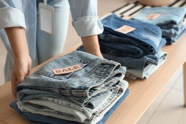 Satış tabelası olan kadın satıcı ve giyim mağazasında katlanmış kot pantolon, yakın plan.