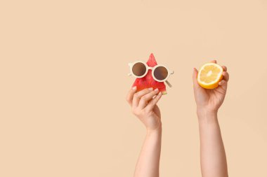 Tatlı karpuz, güneş gözlüğü ve bej arka planda limon parçalı kadın elleri.