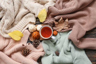 Bir fincan çay, sıcak süveterler, mumlar ve ahşap arka planda sonbahar dekoru olan kompozisyon
