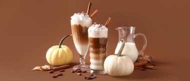 Lezzetli balkabaklı latte, tarçın, sonbahar yaprakları ve kahverengi arka planda bir sürahi süt.