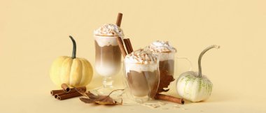 Bir bardak lezzetli balkabaklı latte, tarçın ve bej arka planda sonbahar yaprakları.