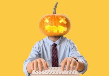 Cadılar Bayramı balkabaklı bir iş adamı sarı arka planda bilgisayar kullanıyor.