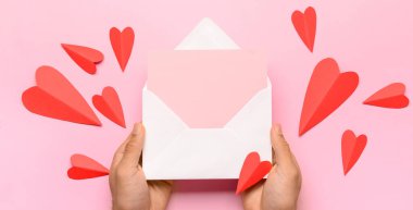 Zarflı eller, boş kart ve pembe arka planda kırmızı kağıt kalpler.