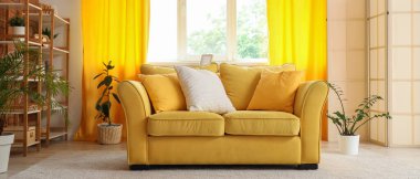 Rahat bir kanepe, ev bitkileri ve oturma odasının içinde sarı perdeler.