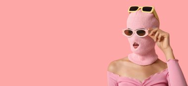 Kar maskeli ve pembe arka planda şık güneş gözlüklü genç bir kadın.