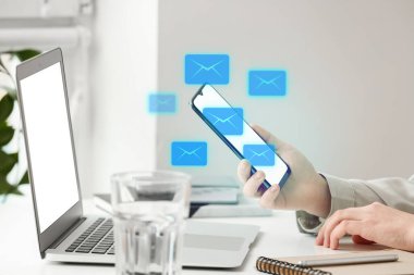 Ofisteki e-postaları kontrol etmek için akıllı telefon ve laptop kullanan bir kadın.