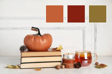 Dekoratif balkabağı, sonbahar yaprakları, kitaplar, mum ve çay ışıklı duvarın yanındaki masada. Farklı renk desenleri