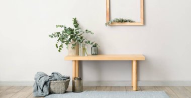 Işık duvarının yanındaki masada yeşil okaliptüs dalları olan vazolar.