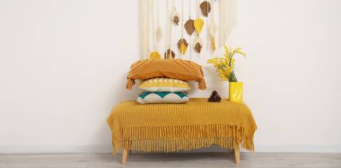 Beyaz duvarın yanındaki bankta çiçek vazosuyla bir yığın yumuşak yastık.