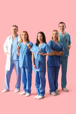 Pembe arka planda kırmızı kurdeleli profesyonel doktor ekibi. Dünya AIDS Günü konsepti