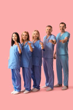 Pembe arka planda kırmızı kurdeleli profesyonel doktor ekibi. Dünya AIDS Günü konsepti