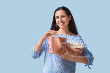 Mavi arka planda patlamış mısır kovaları olan mutlu genç bir kadın.