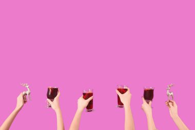 Sıcak şarap kadehleriyle kadın elleri ve pembe arka planda Noel dekoru.