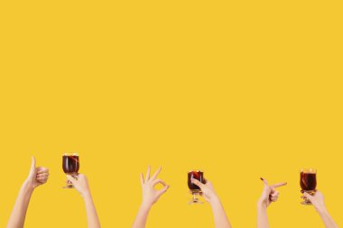 Sarı arka planda sıcak şarap kadehleriyle kadın elleri.