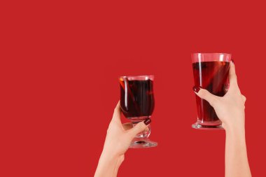 Kırmızı arka planda sıcak şarap kadehleriyle kadın elleri.