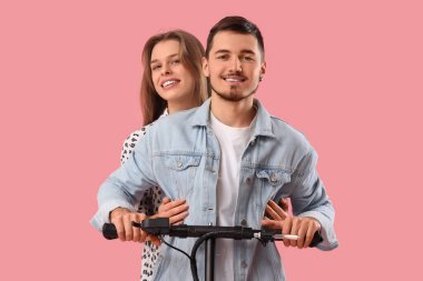 Pembe arka planda elektrikli scooter kullanan genç çift.