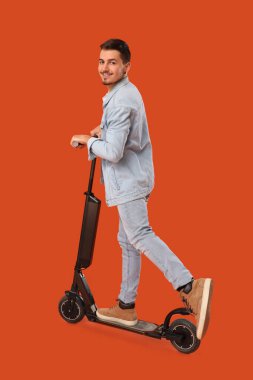 Genç adam turuncu arka planda elektrikli scooter kullanıyor.