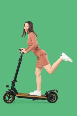 Yeşil arka planda elektrikli scooter süren genç bir kadın.