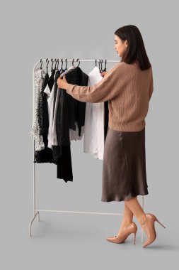 Gri arka planda askıda giysileri olan kadın stilisti