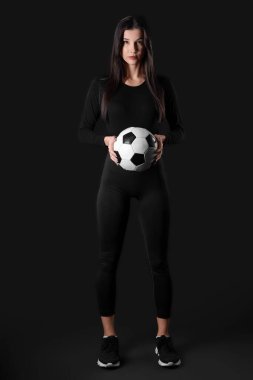 Sporty young woman with soccer ball on black background