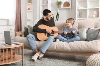Özel müzik öğretmeni oturma odasında gitar dersi veriyor.