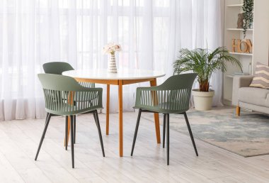 Masası, sandalyeleri, kanepesi, çiçekleri ve raf ünitesi olan modern oturma odasının içinde.