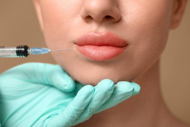 Genç bir kadın kahverengi arka planda dudaklarından enjeksiyon yaptırıyor, yakın plan.
