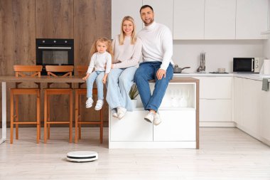 Mutfakta yerde elektrikli süpürgesi olan mutlu bir aile.