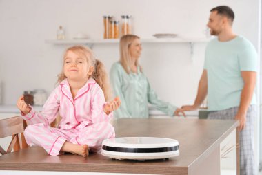 Robot elektrikli süpürgeyle mutfak masasında meditasyon yapan küçük bir kız.