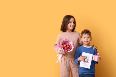 Çiçekli, hediyeli ve portakal rengi duvarın yanında annem için çizim yapan iki kardeş.