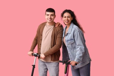 Pembe arka planda modern elektrikli scooterları olan mutlu genç çift.