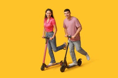 Sarı arka planda modern elektrikli scooter kullanan güzel genç bir çift.